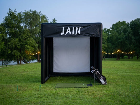  A professional funjain inflatable golf simulator enclosure set up in a luxury backyard at twilight, featuring a high-quality impact screen, premium hitting mat, and golf bag, demonstrating its durability and all-weather performance.