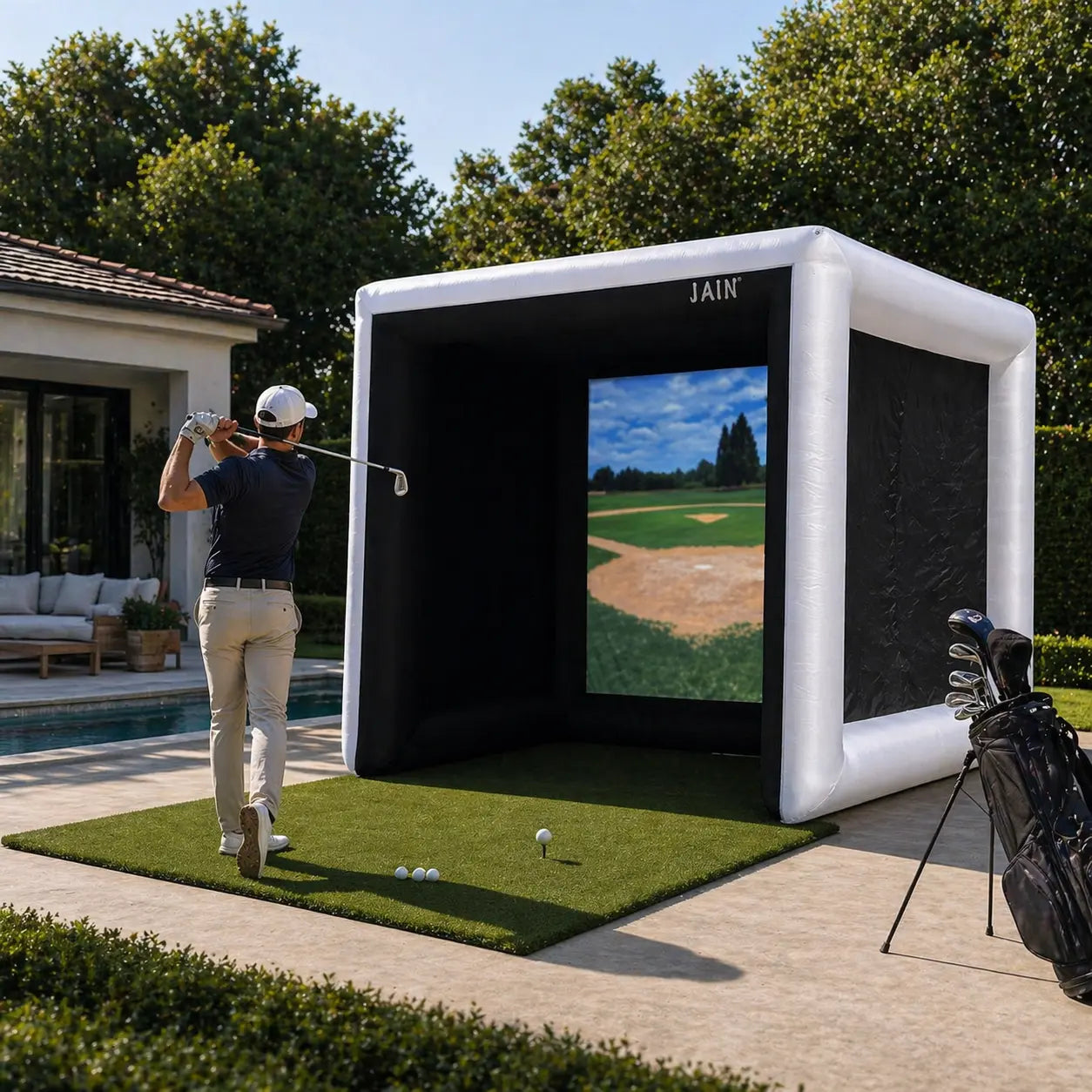 Golfer practicing with a JAIN inflatable golf simulator tent in a backyard setup with hitting mat and golf bag
